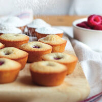 Raspberry financiers on a serving tray being sprinkled by icing sugar