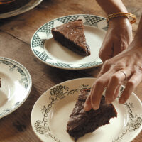 Person putting a slice of chocolate cake on a plate