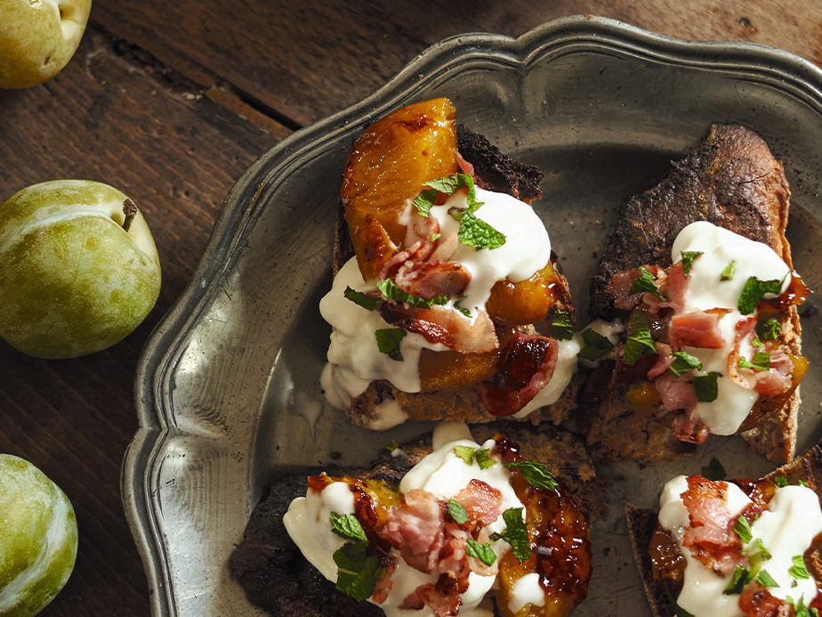 Greengage plum, bacon, and burrata crostini on a plate with apples on the side